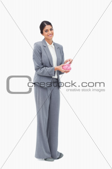 Smiling female banker putting money into piggy bank