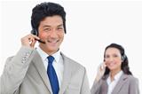 Smiling call center agent with colleague behind him