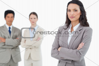 Confident saleswoman with arms folded and colleagues behind her