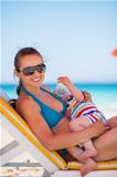 Mother laying on sunbed and holding baby drinking water