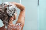 Woman applying shampoo in shower. Rear view