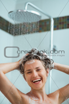 Happy woman applying shampoo in shower