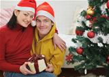Happy young couple with gift sitting near Christmas tree