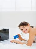 Happy young woman laying on bed with laptop and making online purchases
