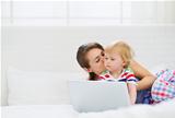 Young mother kissing her modern baby working on laptop