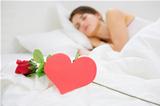 Closeup on red rose and heart shaped postcard near sleeping woman