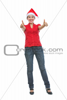 Full length portrait of smiling young woman in Christmas hat showing thumbs up
