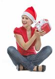 Happy young woman in Christmas hat sitting on floor with present box
