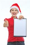 Happy young woman in Christmas hat showing blank clipboard and thumbs up