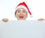 Happy woman in Christmas hat looking out from blank billboard