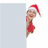 Smiling woman in Christmas hat looking out from blank billboard