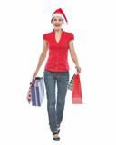 Happy woman in Christmas hat with shopping bags making step forward
