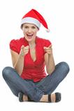 Happy woman in Christmas hat sitting on floor and pointing in camera