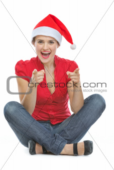 Happy woman in Christmas hat sitting on floor and pointing in camera