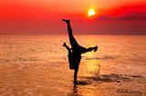 young man hand stand on the beach at sunset