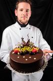 Handsome chef with cake against dark background
