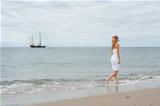 Girl in white dress on the coast with old ship in the background