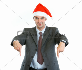 Smiling businessman in Santa's hat pointing down