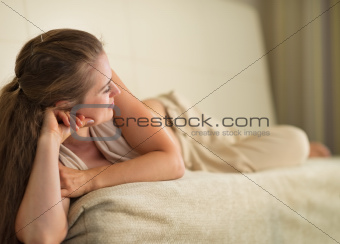 Thoughtful young woman laying on couch and looking on copy space