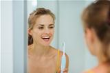 Happy young woman using electric toothbrush in bathroom