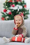 Baby in deer suit with Christmas present box eating cookie