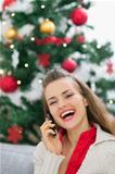 Happy young woman speaking mobile phone near Christmas tree