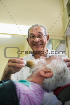 Senior man at work as barber shaving customer 