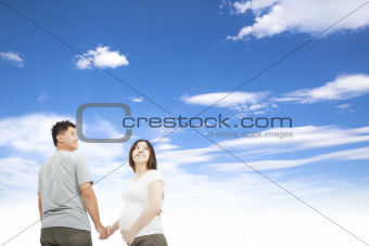 husband holding pregnant wife's hand and cloud background