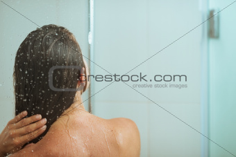 Woman bathing in shower under water jet. Rear view