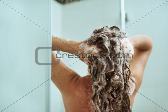Woman washing away shampoo in shower. Rear view