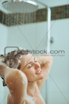 Happy woman washing hair with shampoo in shower
