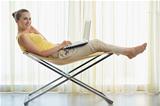 Happy young woman sitting on modern chair and working on laptop