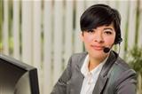 Attractive Young Mixed Race Woman Smiles Wearing Headset Near Computer Monitor.
