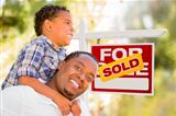 Happy African American Father and Mixed Race Son in Front of Sold Real Estate Sign.