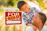 Happy African American Father and Mixed Race Son in Front of Sold Real Estate Sign.