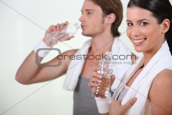 Sporty woman and man drinking water on white background