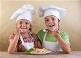 Happy kids with chef hats eating fresh pasta