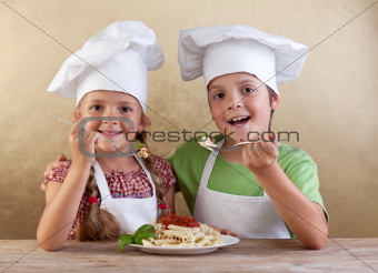 Happy kids with chef hats eating fresh pasta