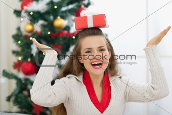 Smiling young woman balancing Christmas present box on head