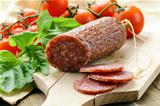 sliced meat sausage salami on wooden board with  green herbs