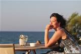 Woman sitting in outdoor cafe with glas of white vine on ocean b