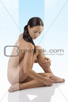  naked brunette sitting on a floor looks down