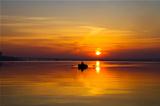 sunset over water surface with small boat