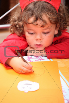 Closeup of a child in a red devil's outfit drawing jack-o-lanterns