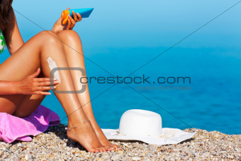 Tan woman applying sunscreen on her legs