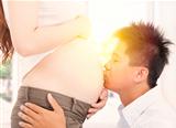 asian father kissing  her pregnant wife's tummy at morning