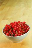 Red currant fruits in a bowl on a wooden table
