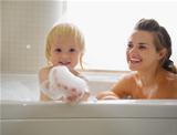 Baby playing with foam while taking bath with mother