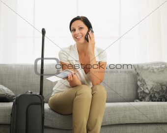 Smiling young woman with passport and air ticket speaking mobile