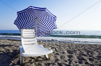 Chaise lounge with an umbrella standing alone on the bank of the blue sea